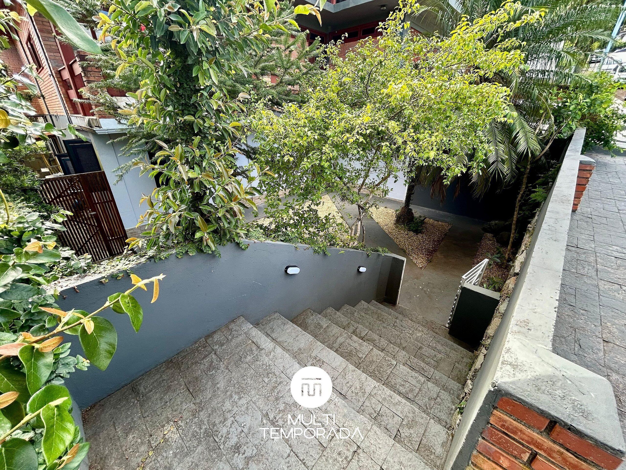 A residential area with a staircase leading to a rooftop garden, surrounded by lush greenery and a modern building facade.