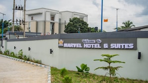 A sign for Marvel Hotel & Suites with a modern building in the background. - MARVEL HOTEL & SUITES LIMITED (Port Harcourt)