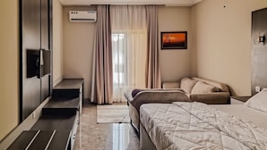 A modern bedroom with a bed, bedside tables, a TV, and a window with curtains. - MARVEL HOTEL & SUITES LIMITED (Port Harcourt)