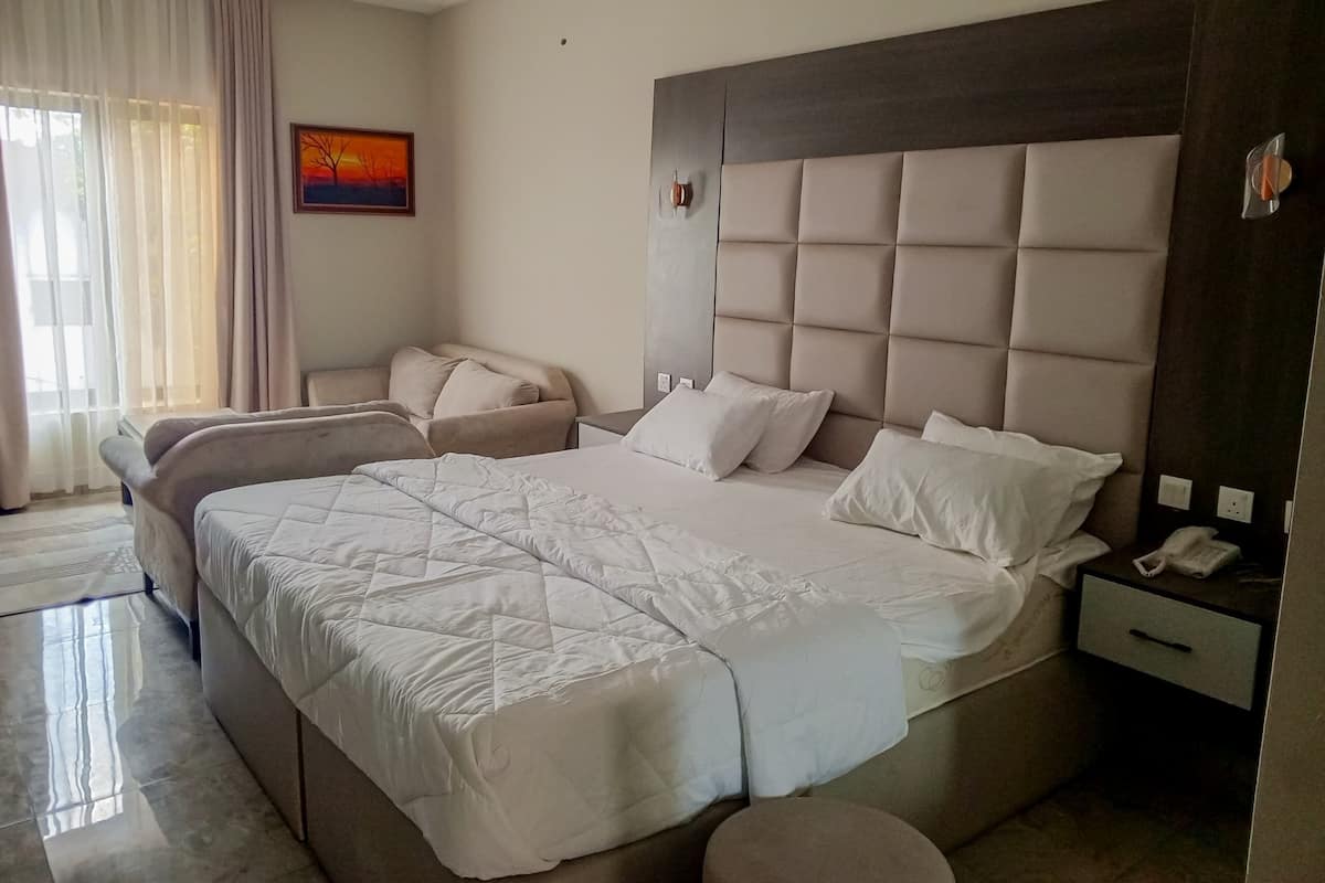 A hotel room with a large bed, a bedside table, a chair, and a painting on the wall.