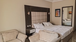 A bedroom with a large bed, two bedside tables, a nightstand, a sofa, and a chair. - MARVEL HOTEL & SUITES LIMITED (Port Harcourt)