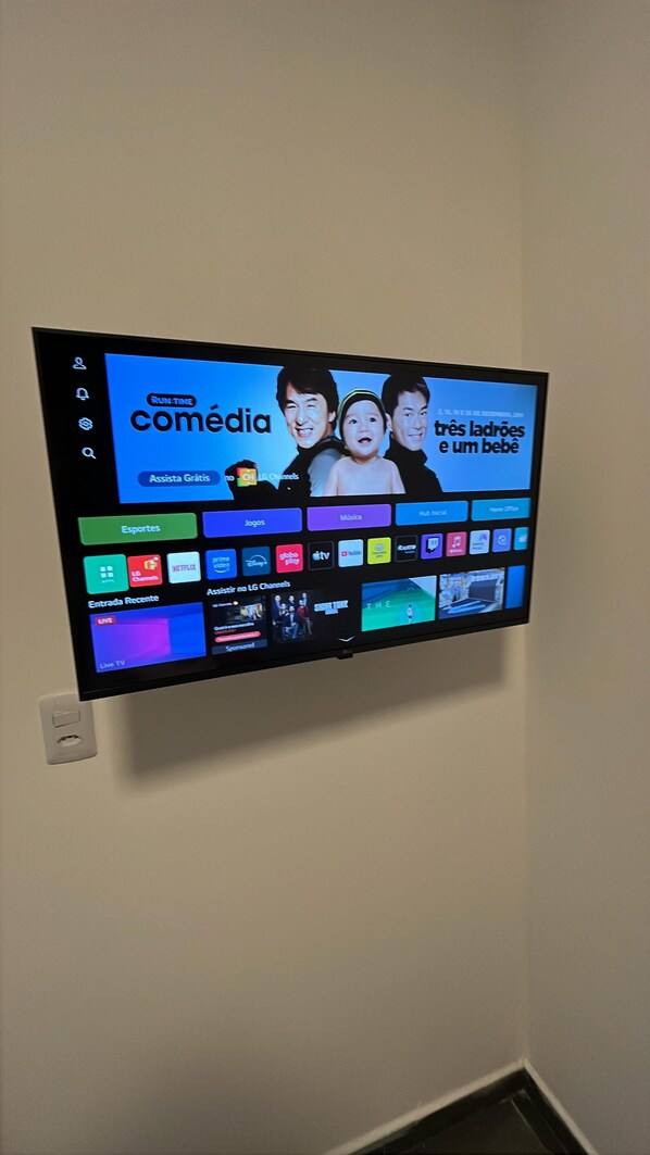 A flat-screen TV mounted on a wall displaying a streaming service interface with various entertainment options. - Hotel Carneiro (Itatiba)