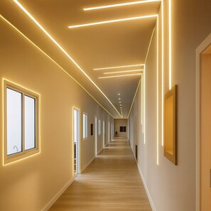 A modern hotel corridor with linear lighting on the ceiling, large windows, and a wooden floor. - Hotel Carneiro (Itatiba)