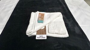 Ein ordentlich bezogenes Bett mit weißen Laken, einer schwarzen Tagesdecke und einem gefalteten Handtuch mit einem Etikett.