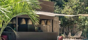 A modern outdoor seating area with a sofa and two chairs, a hanging light fixture, and a bamboo wall. - Villa Pé na Areia com Design Exclusivo (Maraú)