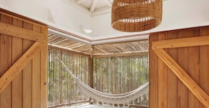 A hammock suspended between wooden beams in a room with a high ceiling and a woven basket hanging from the ceiling. - Villa Pé na Areia com Design Exclusivo (Maraú)