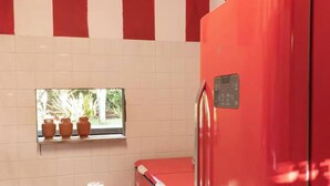 A kitchen with red appliances, white tiled walls, and a window with potted plants.