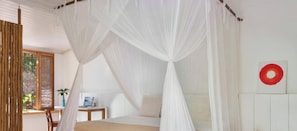 Ein Schlafzimmer mit Himmelbett, einem kleinen Tisch mit Pflanze und einem roten, runden Kunstwerk an der Wand.