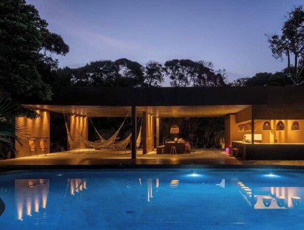 Un espace aménagé au bord de la piscine, comprenant un coin salon couvert, un hamac et un bar.