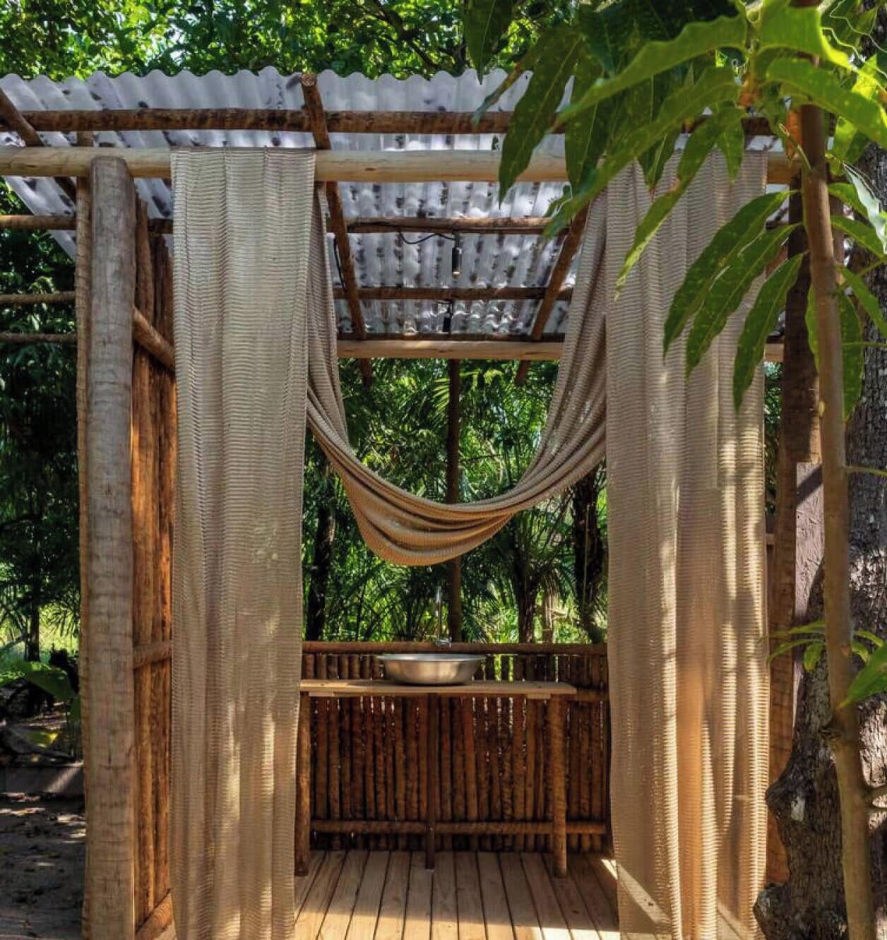 Una hamaca bajo una pérgola con una terraza de madera y un recipiente metálico.