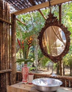 Une salle de bain rustique avec une structure en bois, un lavabo en métal, un miroir décoratif et une plante.