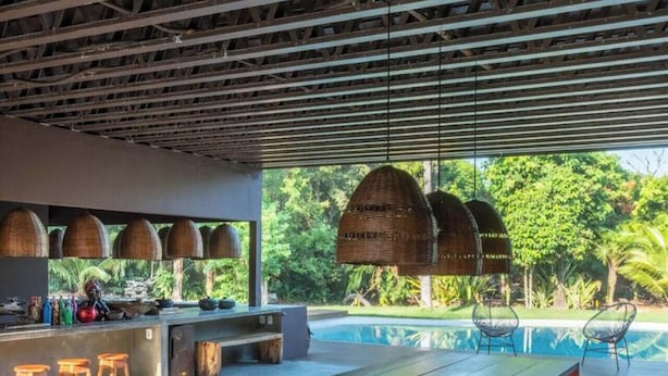 A modern outdoor dining area with a pool view, wooden furniture, and hanging wicker lamps.