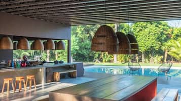 A modern outdoor dining area with a pool view, wooden furniture, and hanging wicker lamps.