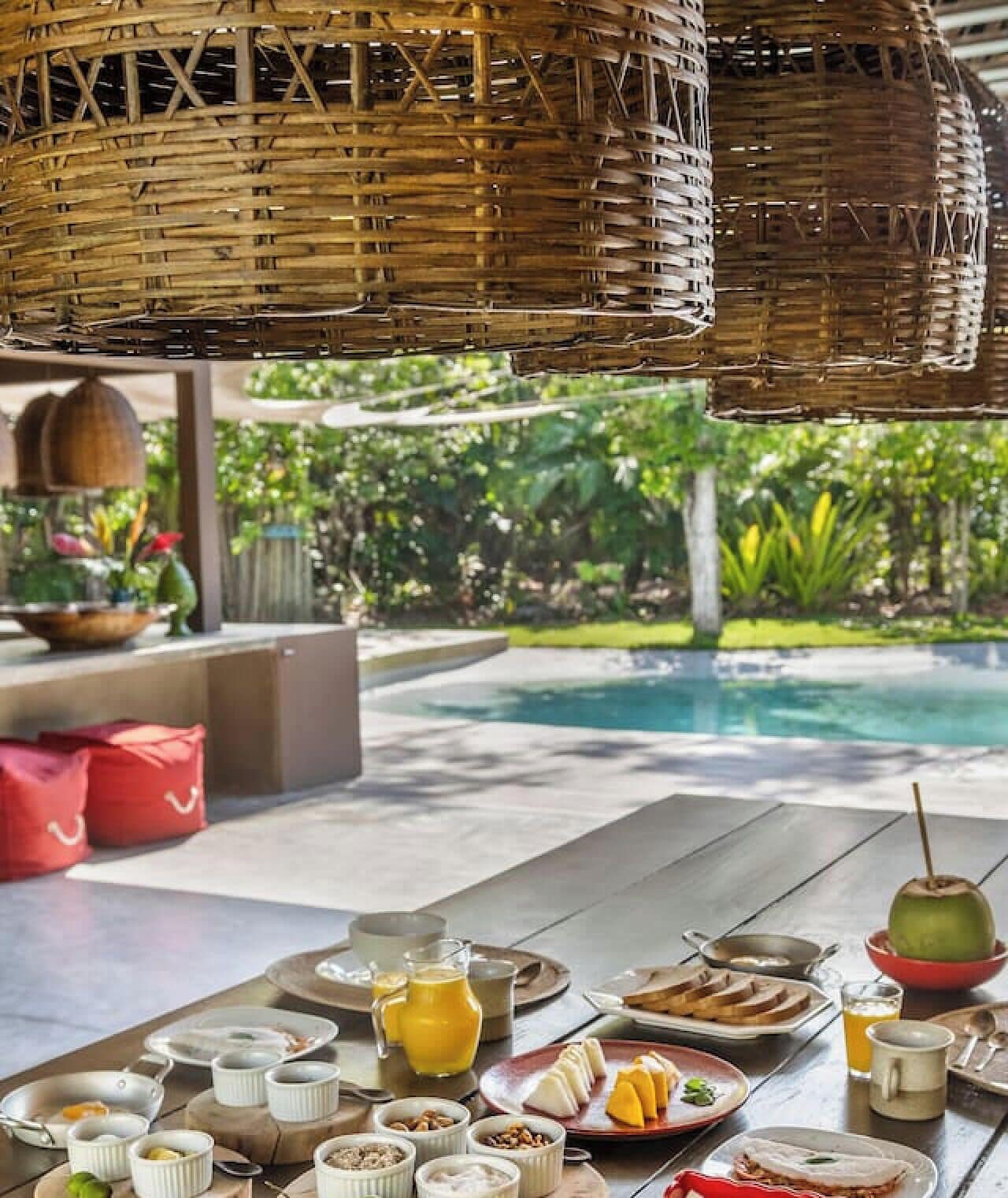 Un desayuno con vistas a la piscina, mobiliario de mimbre y un jardín tropical.