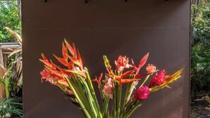 A metal bucket with flowers on a wooden table under a roofed area.