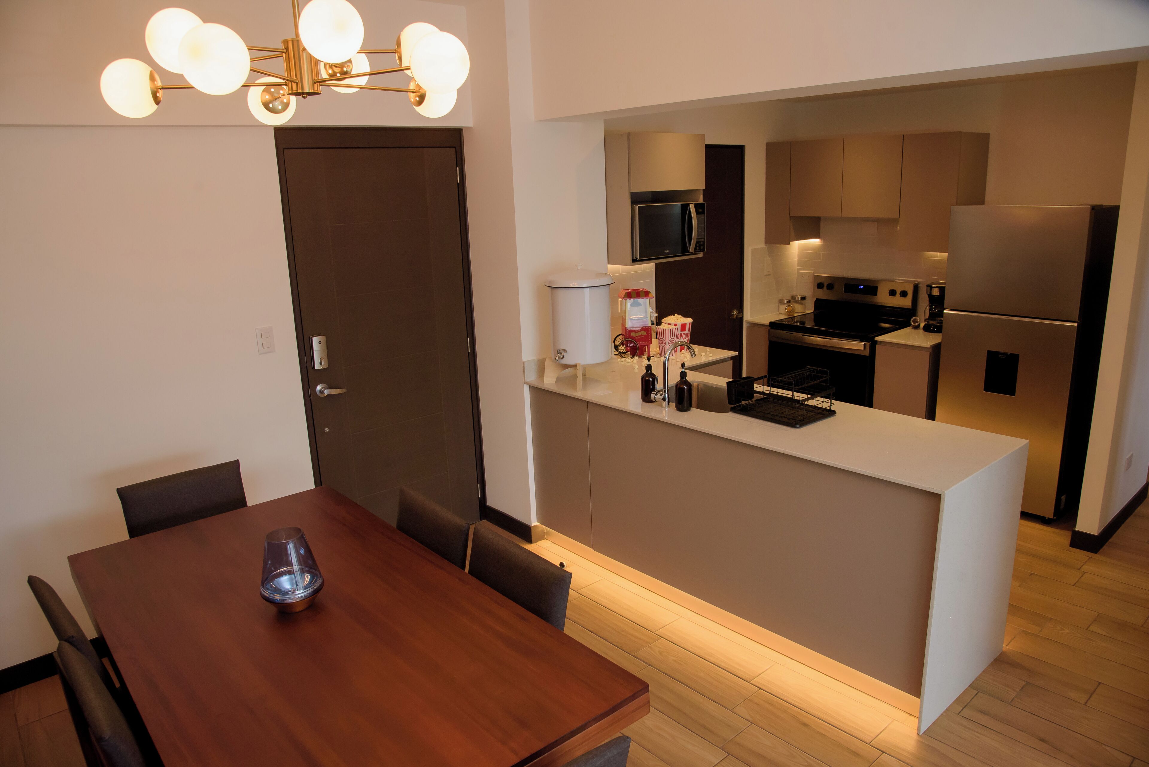 A modern kitchen with a central island, a dining area with a wooden table, and a chandelier.