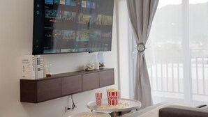 A hotel room with a large flat-screen TV mounted on the wall displaying various streaming services. There is a small table with popcorn containers and a book titled "LONDON the capital of England" on a wooden console table below the TV. - Glam | Modern apartment in exclusive area of Xela (Quetzaltenango)