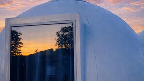 Eine kuppelartige Struktur mit einem großen Fenster, das einen Sonnenuntergang reflektiert.