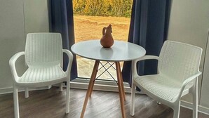 Ein Zimmer mit einem runden Tisch und zwei Stühlen, eine Vase auf dem Tisch und Blick auf Bäume durch ein mit Vorhängen drapiertes Fenster.