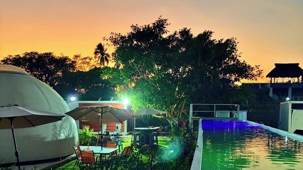 Ein Poolbereich mit Sonnenuntergangsblick, Sitzgelegenheiten im Freien und einem überdachten Bereich mit Sonnenschirmen.