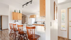 A modern kitchen with wooden cabinets, a central island with bar stools, and a large window providing natural light. - Adventure Retreat - Sunriver/Bachelor/Waterfront (Bend)