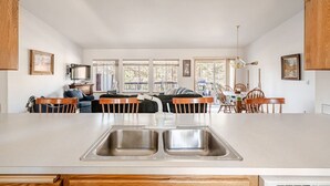 A modern kitchen with a central island, a dining area with wooden chairs, and a sofa in the background. - Adventure Retreat - Sunriver/Bachelor/Waterfront (Bend)