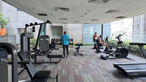 Ett gym med olika typer av träningsredskap, ett mönstrat golv och stora fönster med utsikt över staden.