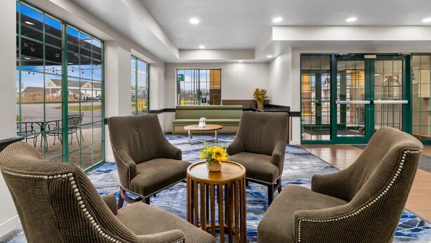 Un hall d’entrée avec quatre fauteuils marron, une table basse ornée d’un vase de fleurs jaunes et un tapis bleu à motifs.