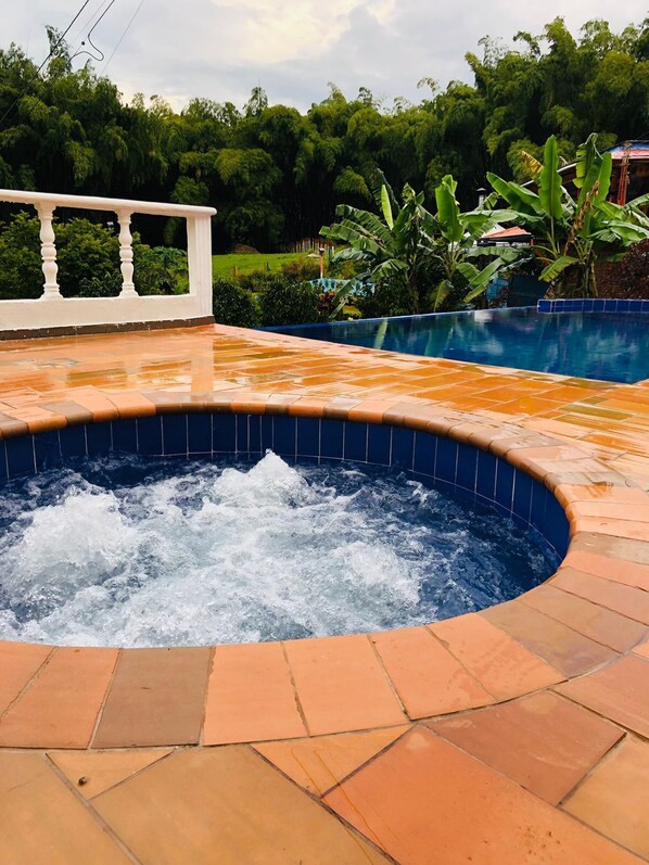 Un jacuzzi con borde de azulejos, rodeado por una zona de patio con baldosas naranjas.