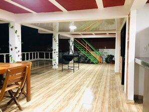 Una habitación amplia con suelo de madera, una mesa de comedor con sillas, una escalera con barandillas de colores y una pared decorada con plantas.