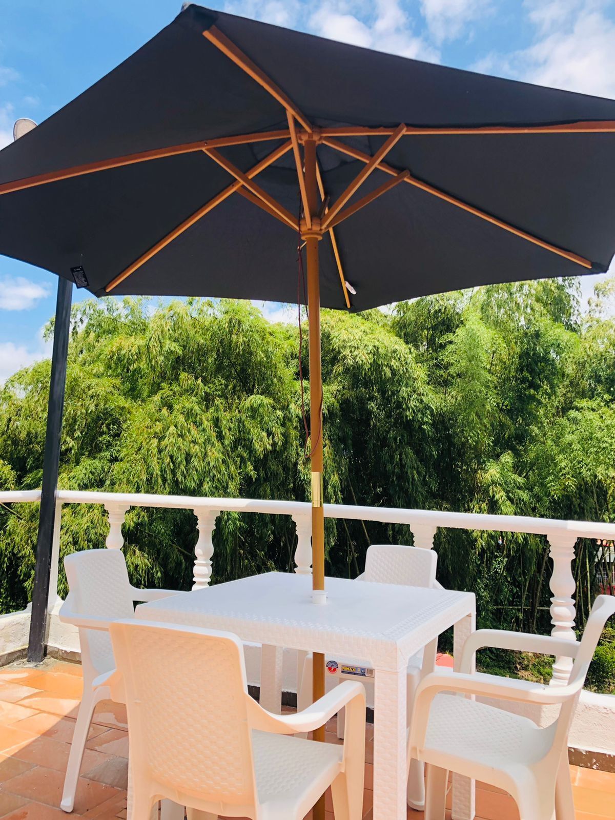 An outdoor patio with a table and chairs, a large umbrella, and a white balustrade.