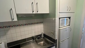 A compact kitchen with white cabinets, a stainless steel sink, a microwave, and a black countertop. - Studio "Foch 22" – Ideal for Spa Guests with Air Conditioning - Conciergerieland (Dax)