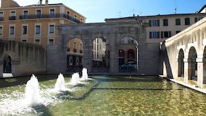A courtyard with a fountain, stone architecture, and buildings with balconies. - Studio "Foch 22" – Ideal for Spa Guests with Air Conditioning - Conciergerieland (Dax)