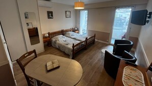 A room with two wooden beds, a dining table, chairs, a small table with a lamp, and a TV mounted on the wall. - Studio "Foch 22" – Ideal for Spa Guests with Air Conditioning - Conciergerieland (Dax)