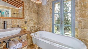 A bathroom with a freestanding bathtub, a large mirror, and a window with a view of trees.