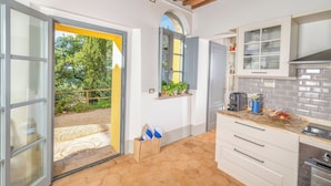 Cozinha com armários brancos, painel de azulejos e janela com vista para um jardim.