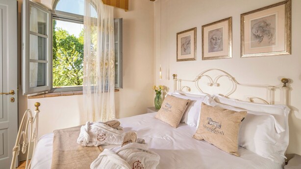 Cama bem arrumada com lençóis brancos e duas almofadas, cabeceira de madeira e janela com persianas azuis.