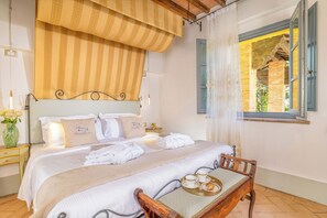A neatly made bed with white linens, a bedside table with a vase of flowers, and a wooden chair with a tray of breakfast items. - Elegant Tuscan Apartment with Fireplace and Countryside Views (Montalcino)
