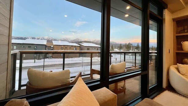 Ein Zimmer mit großem Fenster mit Blick auf eine verschneite Landschaft, einem Sitzplatz auf dem Balkon und einem modernen Interieur.