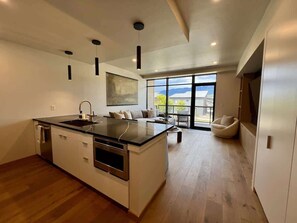 A modern kitchen with a central island, built-in oven, and a dining area with a sofa and chair. - Clubhouse & Pool Amenities, 40 Mins to Glacier NP (Whitefish)