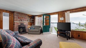 A cozy living room with a fireplace, a sofa, a television, and a view of the lake.