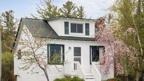 A white two-story house with a front porch, green shutters, and a small garden.