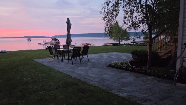 A patio with a table and chairs, a boat docked in the background, and a view of a body of water.