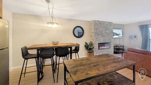 Una sala moderna con chimenea, un comedor con mesa y sillas de madera, y una cocina con refrigerador.