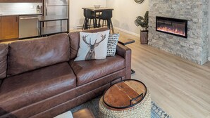 Una sala de estar moderna con un sofá de cuero marrón, una mesa de comedor con sillas, una zona de cocina y una chimenea de piedra.