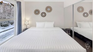 Habitación de hotel con una cama grande, una mesita de noche con lámpara y vistas a un paisaje nevado a través de la ventana.