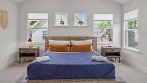 Quarto com cama grande, duas mesas de cabeceira e três janelas.