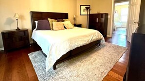 A bedroom with a bed, nightstands, a ceiling fan, a wardrobe, and a door leading to another room. - Quiet, charming 4-bedroom house; 20mins from Atlanta & Airport. (Lithia Springs)