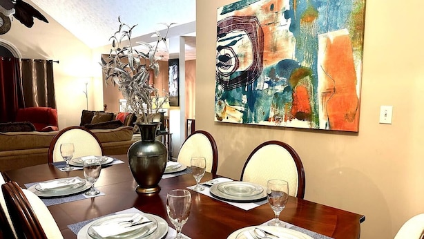 A dining room with a wooden table set for four, a vase with dried plants, and a colorful abstract painting on the wall. - Quiet, charming 4-bedroom house; 20mins from Atlanta & Airport. (Lithia Springs)