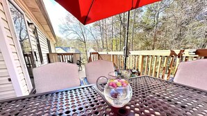 A patio with a metal table and chairs, a pitcher of fruit, and a red umbrella. - Quiet, charming 4-bedroom house; 20mins from Atlanta & Airport. (Lithia Springs)